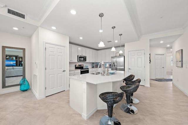 kitchen with appliances with stainless steel finishes, a kitchen island with sink, sink, white cabinets, and hanging light fixtures