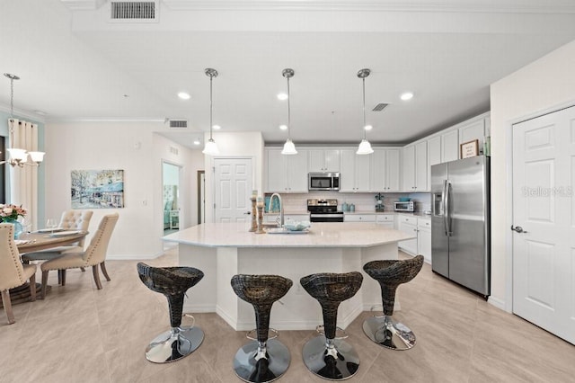 kitchen with white cabinets, decorative light fixtures, stainless steel appliances, and an island with sink