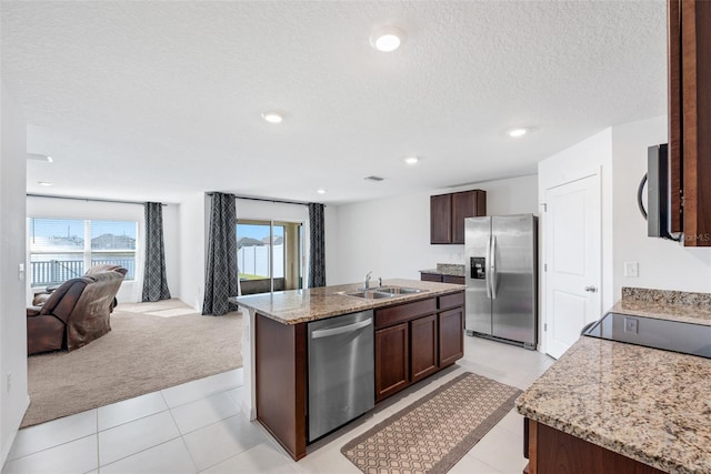 kitchen with appliances with stainless steel finishes, a textured ceiling, light colored carpet, sink, and an island with sink