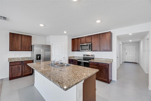 kitchen with appliances with stainless steel finishes, light stone counters, a kitchen island with sink, sink, and light tile patterned floors