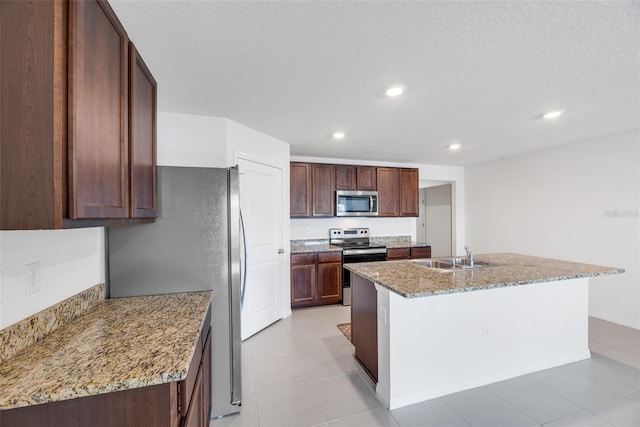 kitchen featuring light stone counters, sink, stainless steel appliances, and a center island with sink