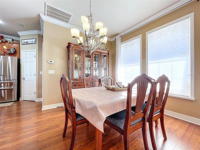 dining space with wood-type flooring, crown molding, and a notable chandelier