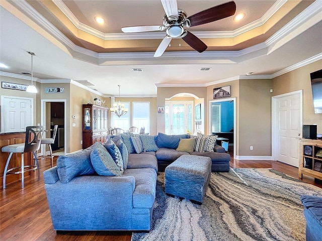 living room with ceiling fan with notable chandelier, dark hardwood / wood-style flooring, a tray ceiling, and crown molding