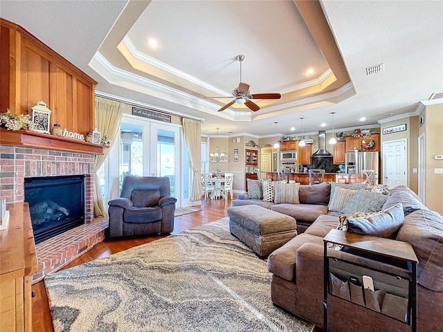 living room featuring ceiling fan, a brick fireplace, wood-type flooring, a tray ceiling, and ornamental molding