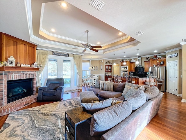 living room featuring ceiling fan, a brick fireplace, crown molding, hardwood / wood-style floors, and a tray ceiling