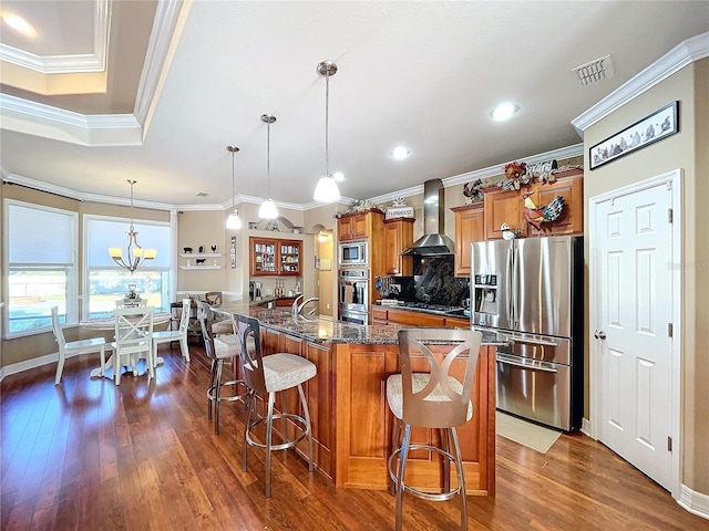 kitchen featuring a kitchen breakfast bar, stainless steel appliances, wall chimney range hood, decorative light fixtures, and a kitchen island