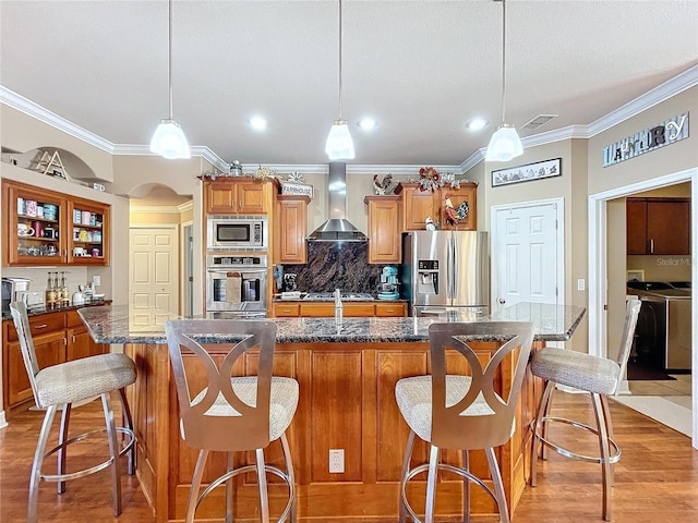 kitchen featuring a center island, wall chimney exhaust hood, decorative light fixtures, a kitchen bar, and stainless steel appliances