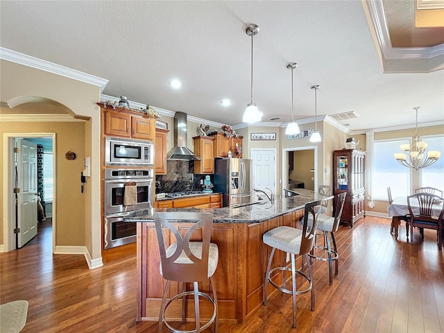 kitchen featuring wall chimney exhaust hood, a breakfast bar, stainless steel appliances, a spacious island, and pendant lighting