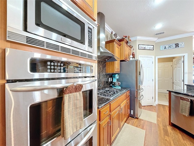 kitchen with stainless steel appliances, wall chimney range hood, ornamental molding, decorative backsplash, and light wood-type flooring