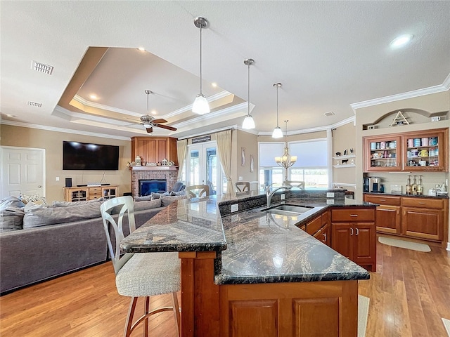 kitchen featuring ceiling fan with notable chandelier, a tray ceiling, a large island, sink, and a breakfast bar area