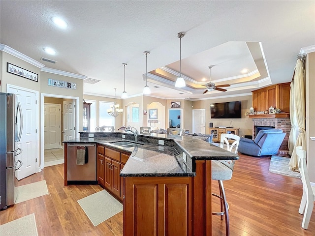 kitchen with ceiling fan with notable chandelier, a raised ceiling, ornamental molding, and stainless steel appliances