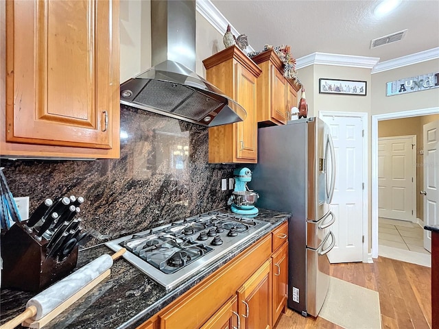 kitchen with stainless steel appliances, wall chimney range hood, backsplash, crown molding, and light hardwood / wood-style floors