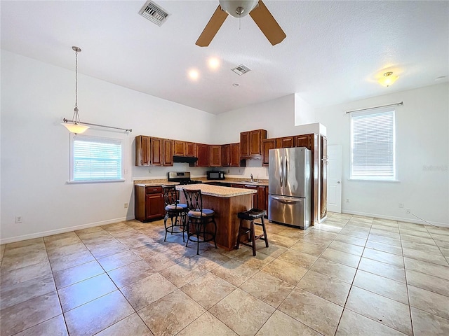 kitchen featuring ceiling fan, decorative light fixtures, a breakfast bar area, a kitchen island, and appliances with stainless steel finishes