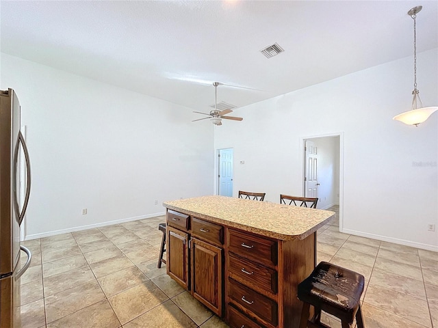 kitchen with stainless steel refrigerator, ceiling fan, a center island, decorative light fixtures, and a breakfast bar