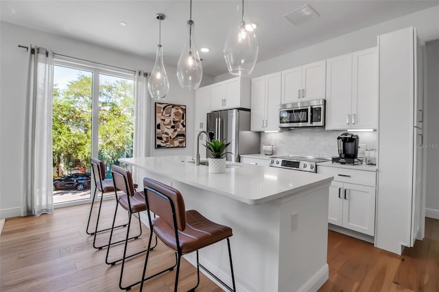 kitchen featuring a kitchen breakfast bar, an island with sink, stainless steel appliances, light countertops, and tasteful backsplash