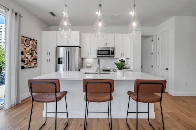 kitchen featuring visible vents, light wood-style floors, backsplash, an island with sink, and appliances with stainless steel finishes