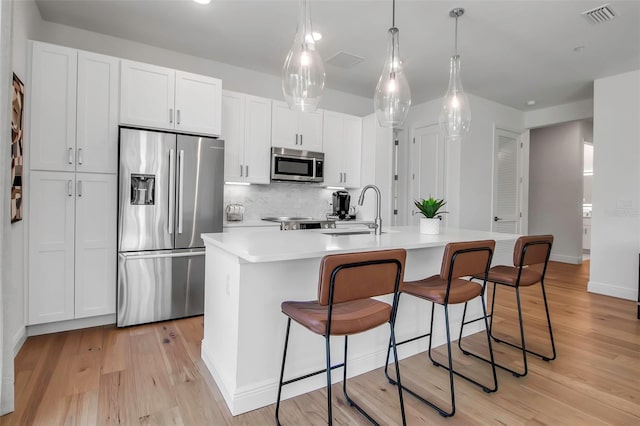 kitchen with a sink, light wood-style flooring, backsplash, appliances with stainless steel finishes, and visible vents