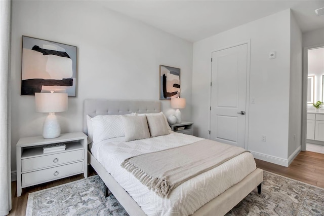 bedroom with connected bathroom, baseboards, and wood finished floors