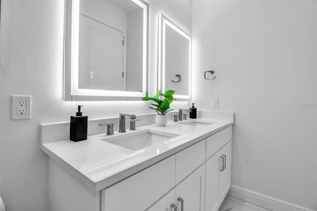 bathroom featuring marble finish floor, baseboards, a sink, and double vanity