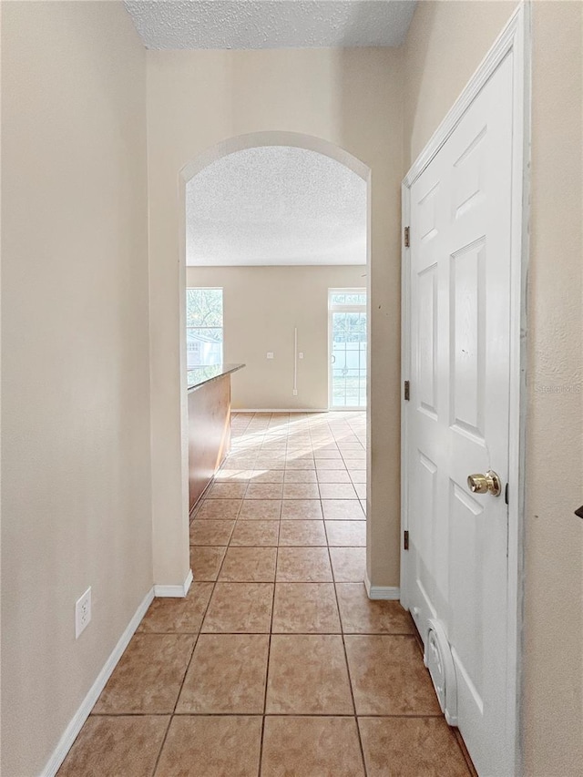 hall with light tile patterned floors, a textured ceiling, and a wealth of natural light