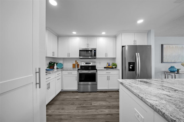 kitchen with white cabinets, decorative backsplash, light stone counters, appliances with stainless steel finishes, and dark hardwood / wood-style flooring