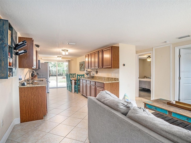 kitchen with light tile patterned flooring, light stone countertops, ceiling fan, and a textured ceiling