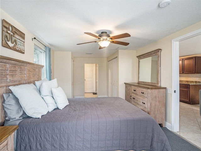 tiled bedroom with a closet, a textured ceiling, ceiling fan, and ensuite bath