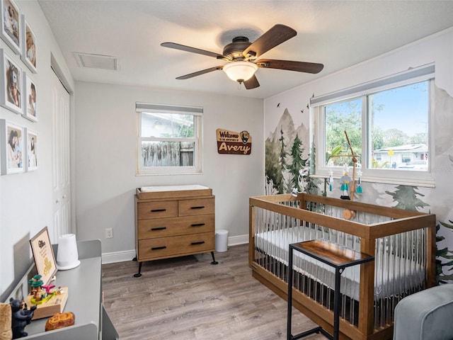 bedroom with a crib, light hardwood / wood-style floors, multiple windows, and a closet