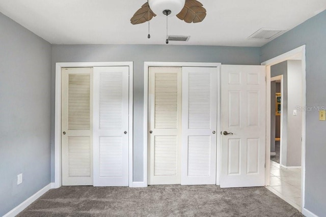 unfurnished bedroom with ceiling fan, light carpet, and two closets