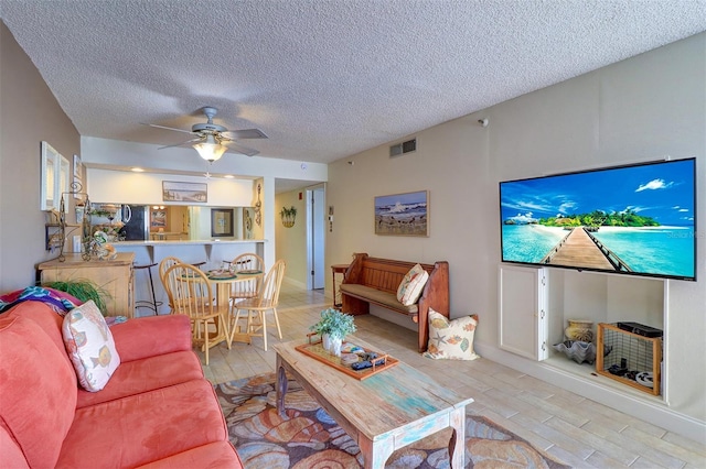 living room featuring ceiling fan, light hardwood / wood-style floors, and a textured ceiling