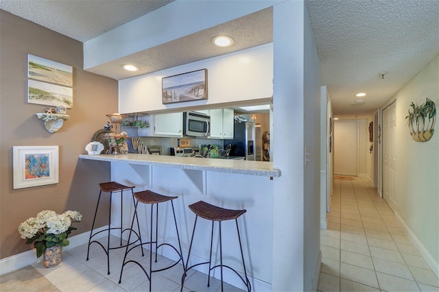 kitchen with stainless steel appliances, light tile patterned floors, kitchen peninsula, a kitchen bar, and white cabinets