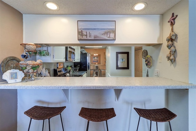 kitchen with appliances with stainless steel finishes, a textured ceiling, and a breakfast bar area