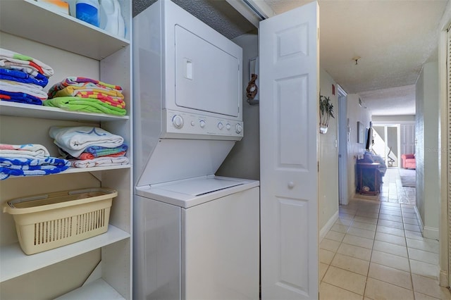 laundry area featuring a textured ceiling, light tile patterned flooring, and stacked washer / dryer