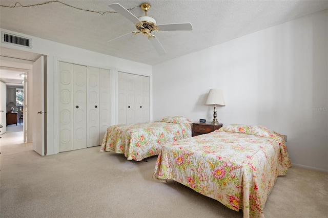 carpeted bedroom with ceiling fan, a textured ceiling, and two closets