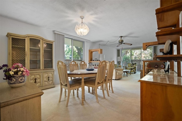 dining space featuring plenty of natural light, light colored carpet, ceiling fan with notable chandelier, and a textured ceiling