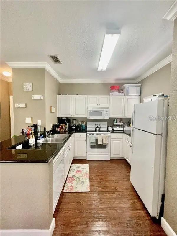 kitchen with white cabinetry, sink, kitchen peninsula, white appliances, and ornamental molding