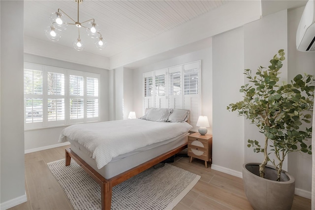 bedroom with a wall unit AC, light hardwood / wood-style floors, a chandelier, and multiple windows