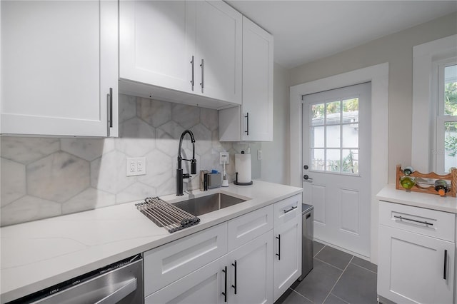 kitchen with stainless steel dishwasher, dark tile patterned floors, backsplash, white cabinetry, and sink