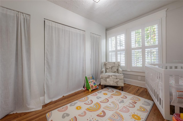 bedroom featuring a crib, wood-type flooring, and a textured ceiling