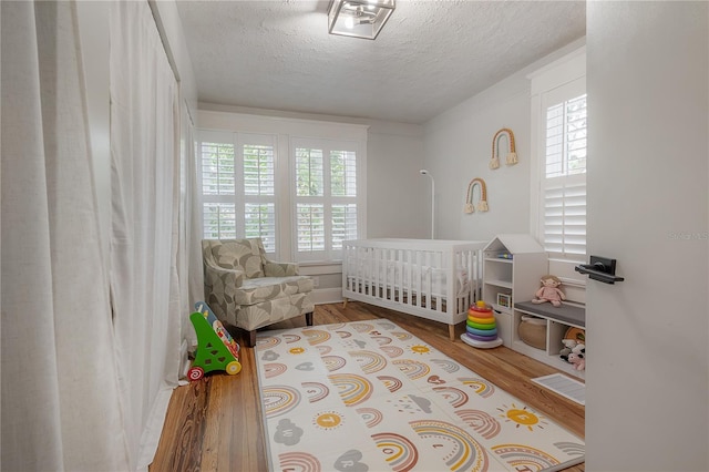 bedroom featuring hardwood / wood-style flooring, a textured ceiling, a crib, and multiple windows