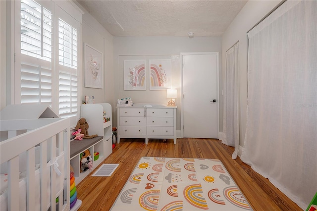 bedroom featuring a crib, a textured ceiling, and light hardwood / wood-style flooring