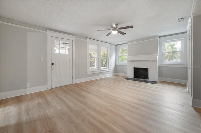 unfurnished living room with light hardwood / wood-style floors, a fireplace, ceiling fan, and a textured ceiling