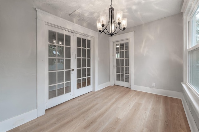 unfurnished dining area featuring light hardwood / wood-style flooring, french doors, and an inviting chandelier