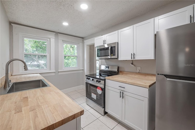 kitchen with a textured ceiling, stainless steel appliances, wooden counters, white cabinetry, and sink