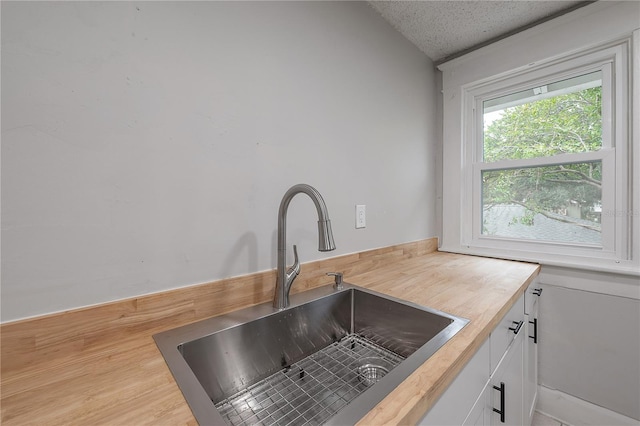 kitchen with sink, a textured ceiling, white cabinetry, and wood counters