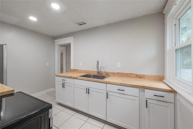 kitchen with sink, white cabinets, light tile patterned flooring, wooden counters, and range with electric stovetop