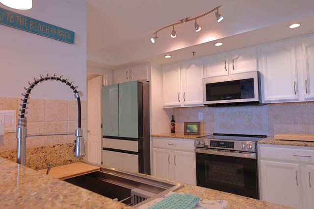 kitchen featuring white cabinets, appliances with stainless steel finishes, tasteful backsplash, and light stone counters