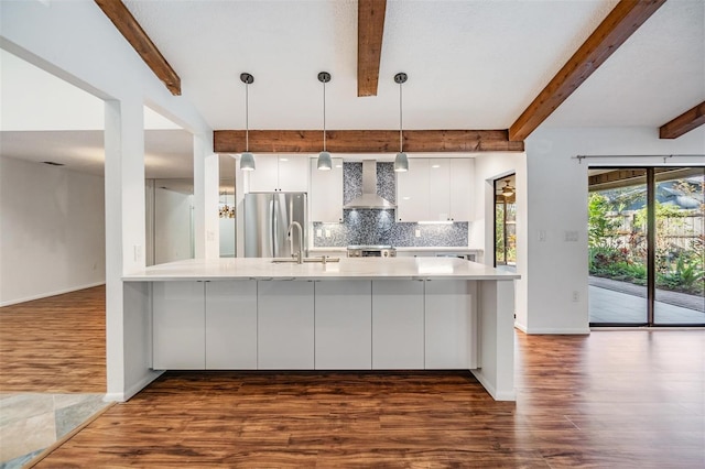 kitchen with white cabinetry, stainless steel fridge, backsplash, hanging light fixtures, and wall chimney exhaust hood