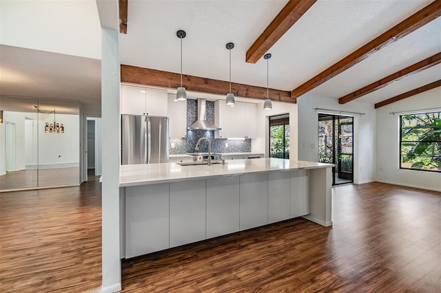 kitchen featuring pendant lighting, white cabinets, stainless steel fridge, decorative backsplash, and wall chimney exhaust hood