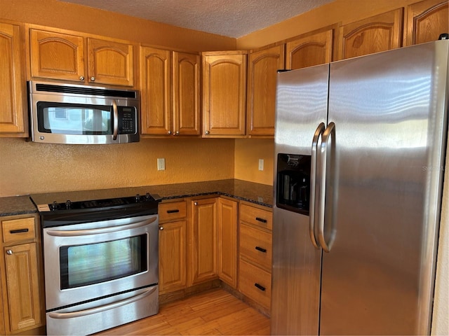 kitchen featuring dark stone countertops, light hardwood / wood-style flooring, a textured ceiling, and appliances with stainless steel finishes